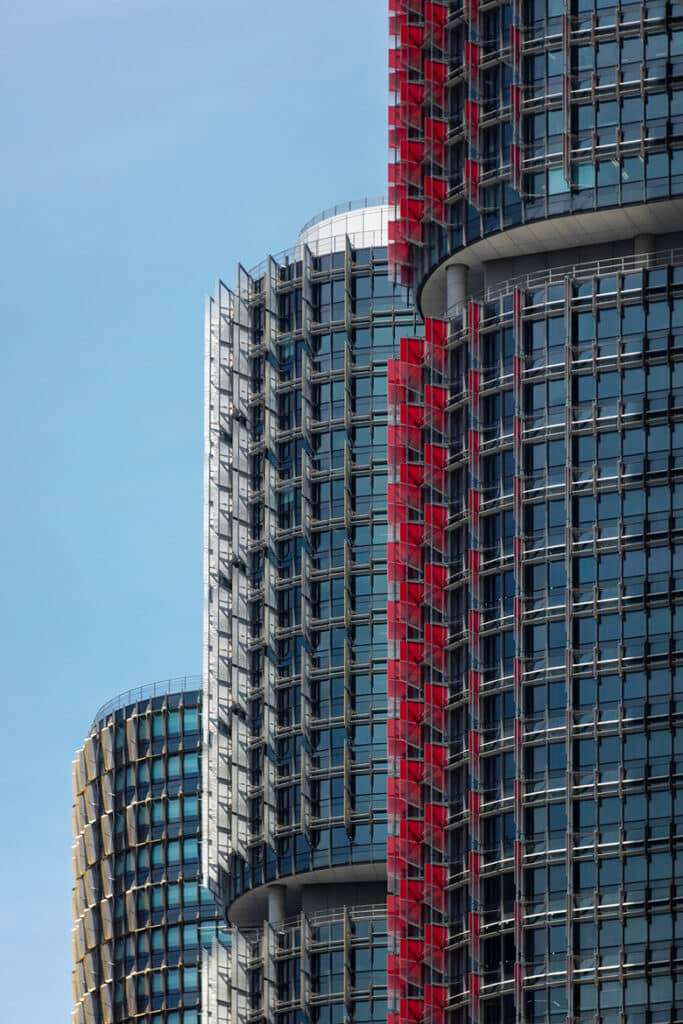 Close-up of Barangaroo&rsquo;s towers: curved glass facades with bold red accents against a clear blue sky.