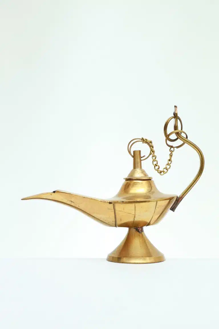Elegant golden Aladdin's lamp with intricate handle on a clean white backdrop.