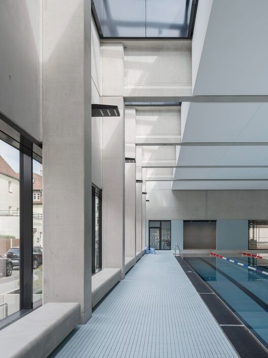 Indoor swimming pool at Sportbad am Rabet project in Leipzig, showing modular design, use of glass and exposed concrete, and open spaces integrated with nature and urban context.