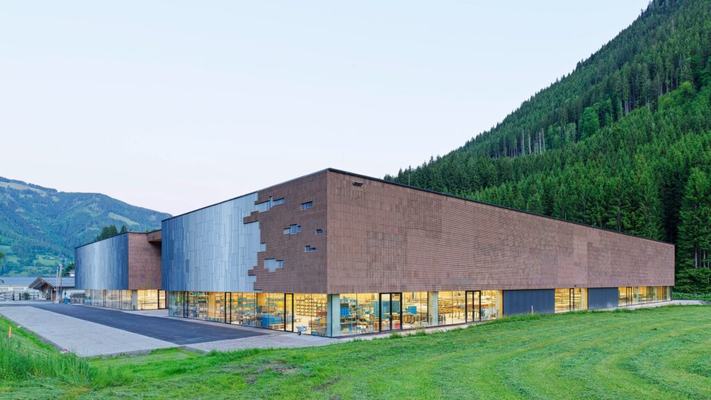 هول هجين من الخشب والخرسانة في النمسا، يندمج مع التلال الغابية بواجهة متنوّعة وأرضية زجاجية مضيئة.