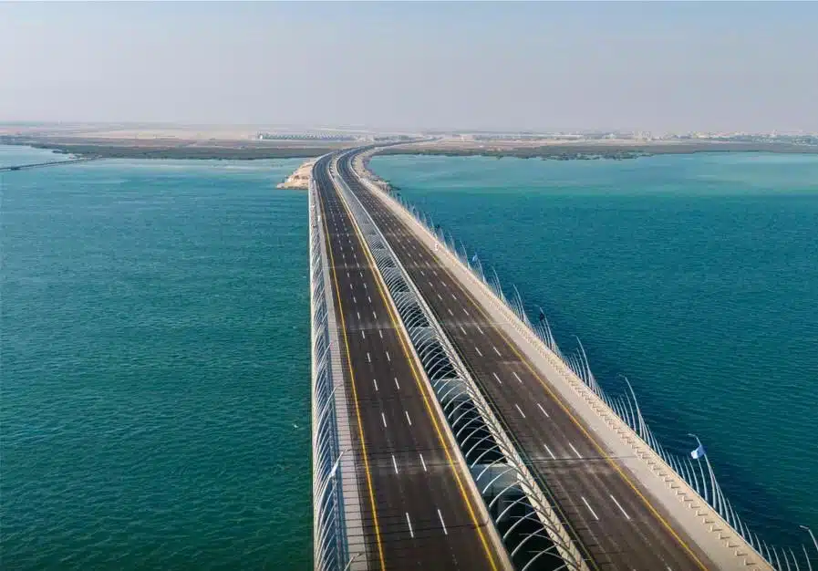 A sleek bridge gliding over turquoise waters, its curves and reflections evoke fluid motion and coastal harmony.
