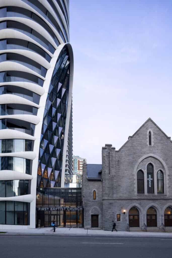برج حديث منحني، واجهة كنيسة حجرية تاريخية، مدخل زجاجي، حركة دمج حضري.