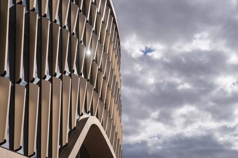Precision glass facade interacting with sunlight and shifting clouds, feels alive.