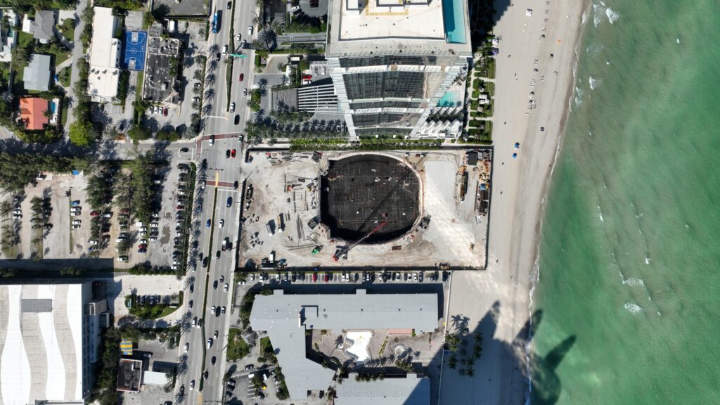 Massive concrete base anchors future tower on beachfront, blending motion and precision.