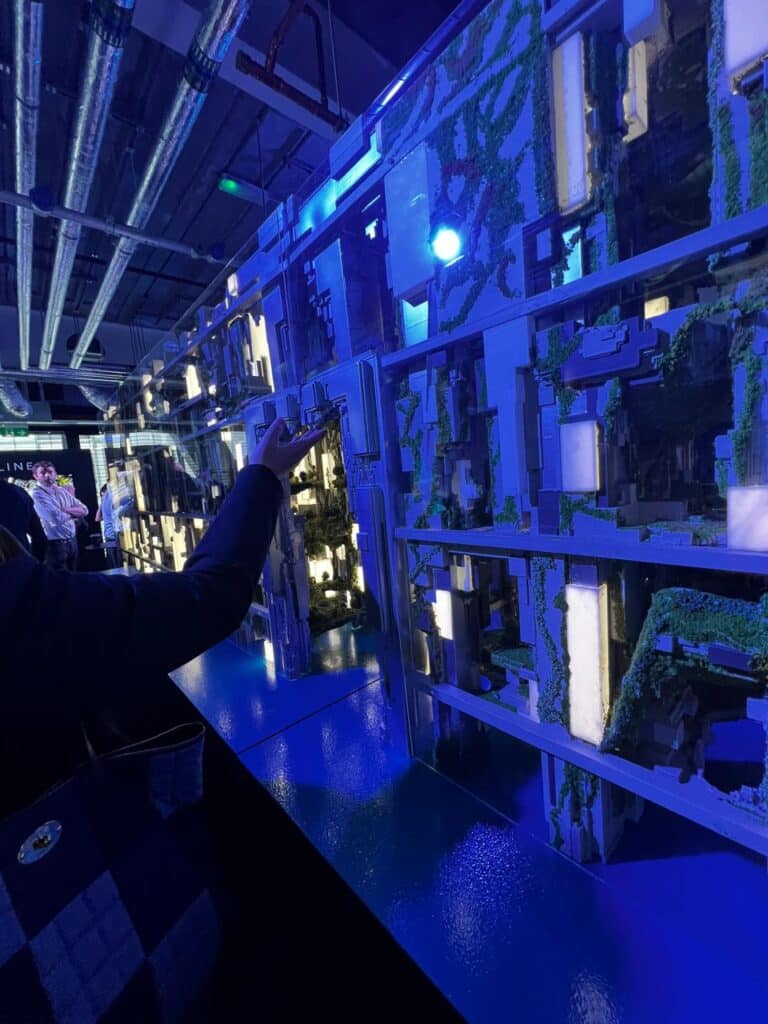 An illuminated architectural model of The Line, showcasing its vertical design and green spaces, with a visitor interacting during an exhibition.