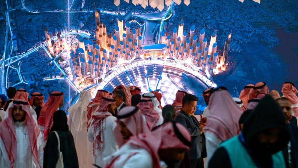 Visitors gaze at a glowing city model, where towers gleam and lights flow seamlessly between open spaces.