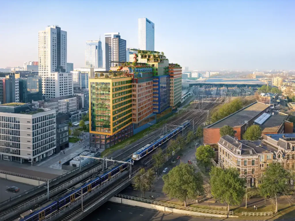 Towering structure beside railway tracks, blending bold colors with rooftop greenery.