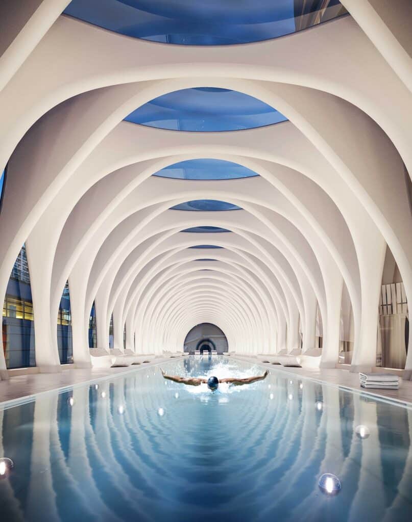 مسبح 50 مترًا معلق، أضلاع هيكلية بيضاء مقوسة، إضاءة داخلية هادئة، انعكاسات مائية.