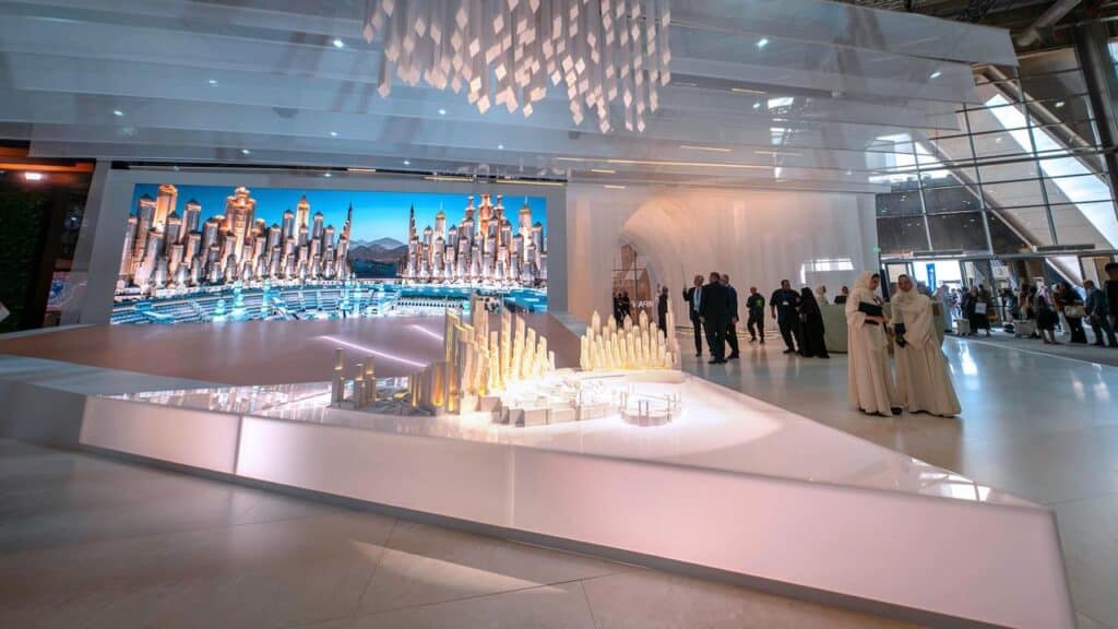 ضوء ناعم ينساب على النموذج المعماري، وزوار يتأملون التفاصيل بين المساحات المفتوحة والمقنّعة.