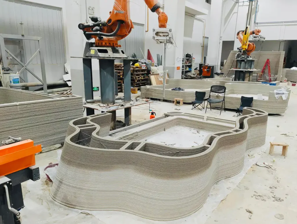 روبوتات طباعة ثلاثية الأبعاد في ورشة العمل تُنتج أجزاءً خرسانية عضوية لمشروع ديزرت آرك، تُظهر الطبقات المتدرجة التي تشبه تكوينات الرمال.