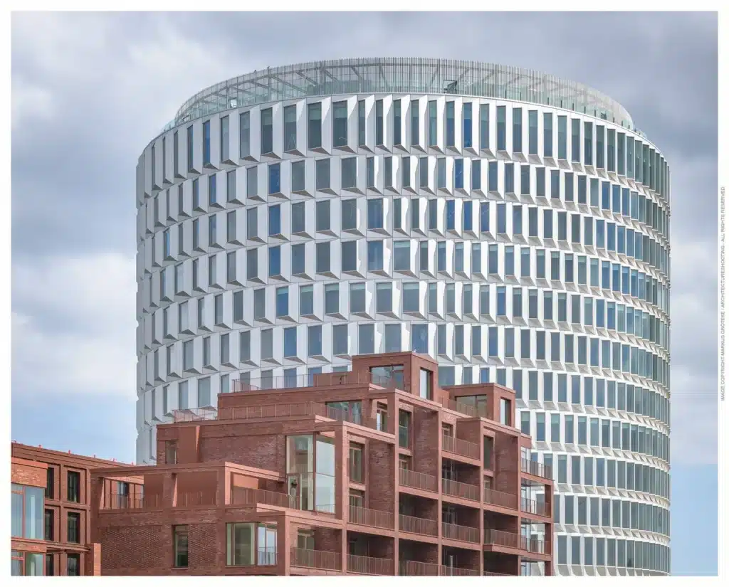 مبنى قمة نوردو الأسطواني الأبيض يرتفع خلف مبانٍ سكنية من الطوب الأحمر، في مشهد يجمع بين الحداثة والتراث المعماري.