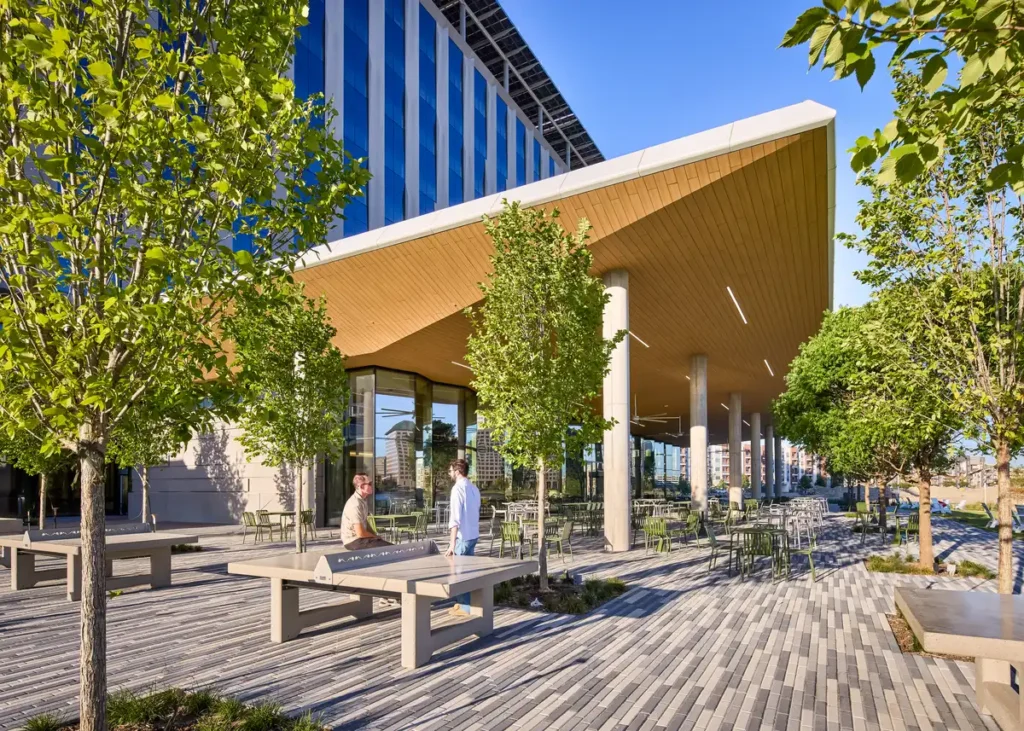 فناء خارجي يجمع بين الخشب والخرسانة، تحت ظل الأشجار الخضراء.