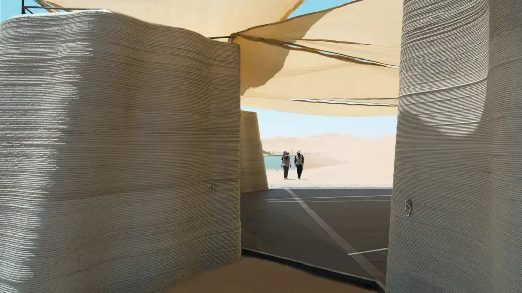 Inside Desert Ark, layered 3D printed walls frame a view of two visitors walking under fabric canopies toward the desert horizon.
