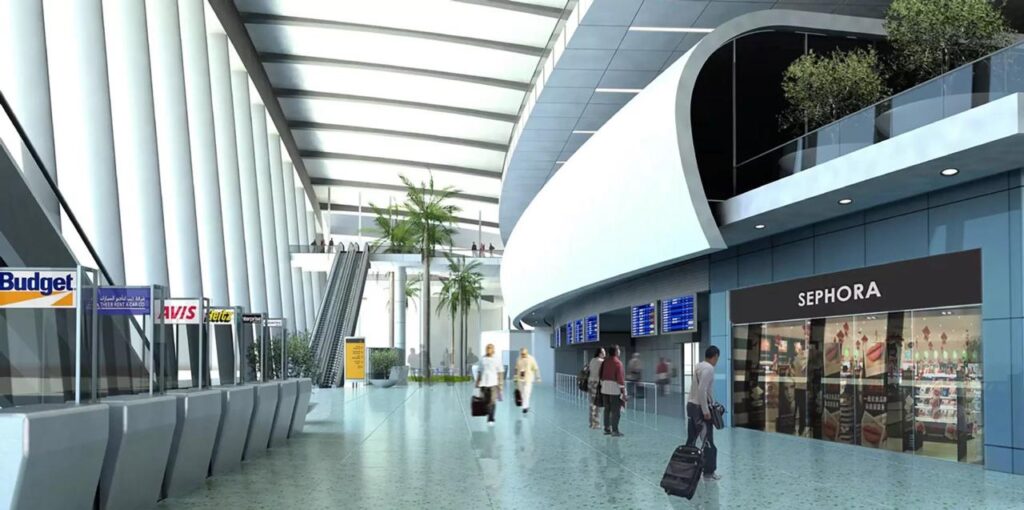 مشهد داخلي لمطار جازان مساحة واسعة، سقف عالٍ، نخيل، ومحلات تجارية