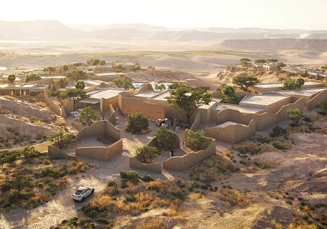 Earthen structures blend into the dunes, softened by trees that add natural warmth.