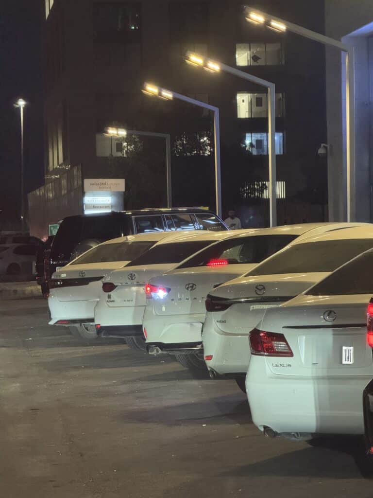 Row of white cars parked tightly bumper-to-bumper in an urban setting at night, illustrating parking scarcity and urban congestion.