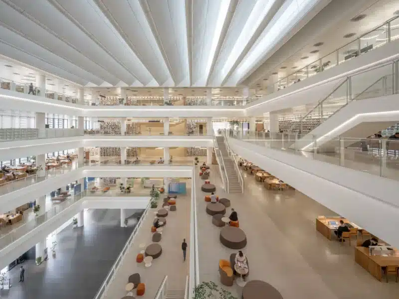 The interior hall of the Shenzhen Cultural Library featuring a multi-level open layout filled with natural light from the skylit ceiling.