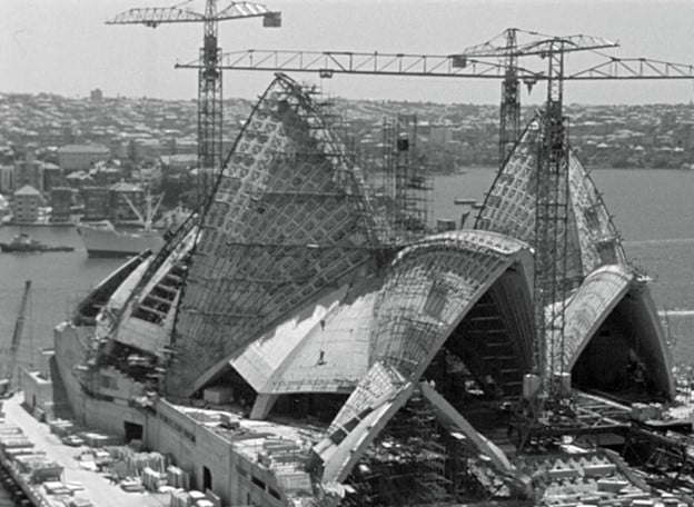 Sydney Opera House under construction with cranes and exposed shell structures.