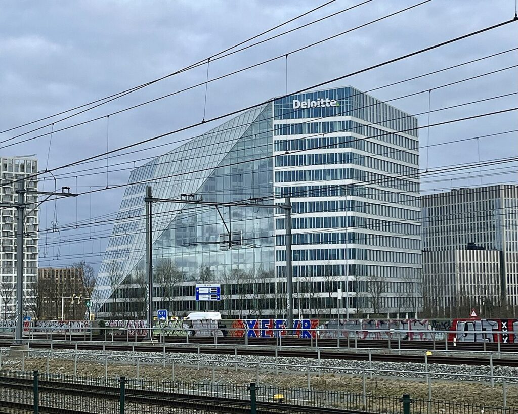 مبنى مكاتب زجاجي حديث يُعرف باسم "ذا إيدج" في أمستردام، يتميز بواجهة مائلة وتصميم يعتمد على كفاءة الطاقة.