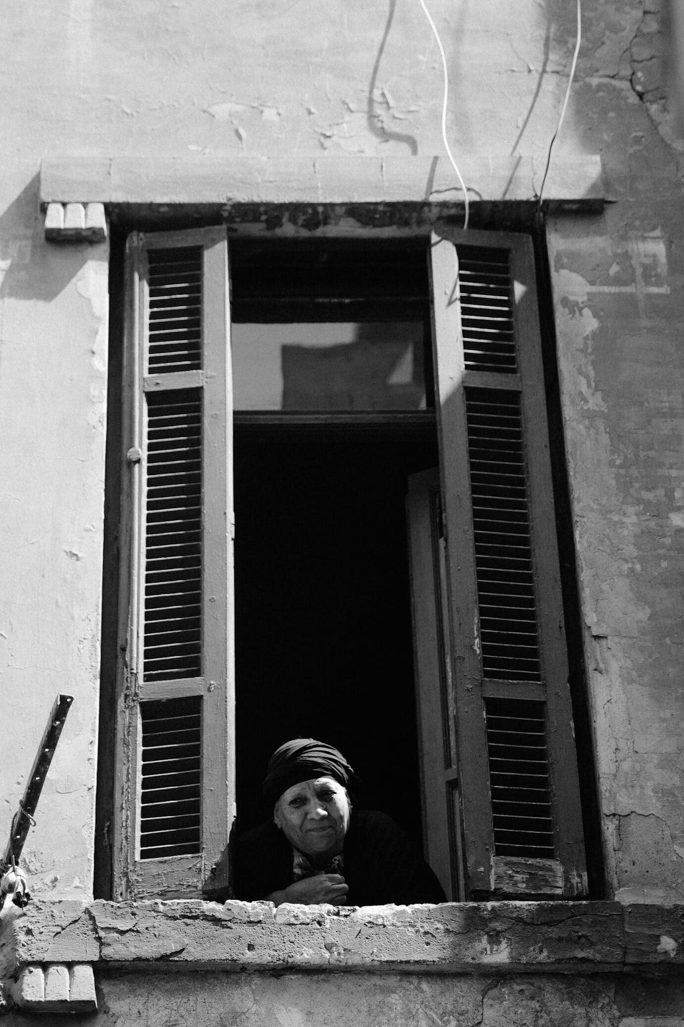 A black and white portrait of a woman gazing from a window in Cairo's historic district.