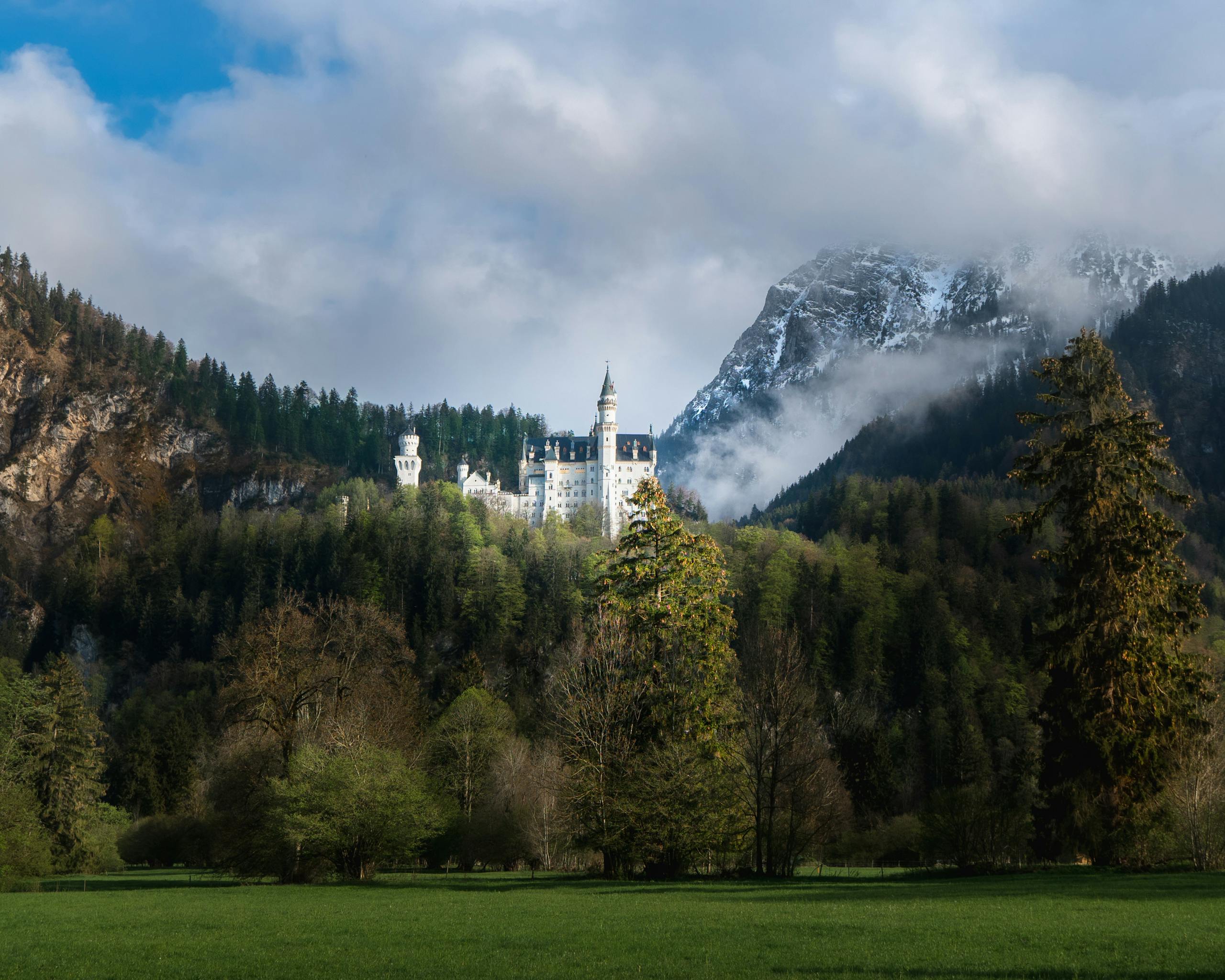 A majestic view of Neuschwanstein Castle in Germany, framed by lush greenery and mountains.