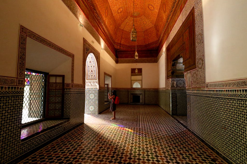 A person in a traditional Moroccan hall with ornate tilework and stained glass at Bahia Palace, Marrakech.