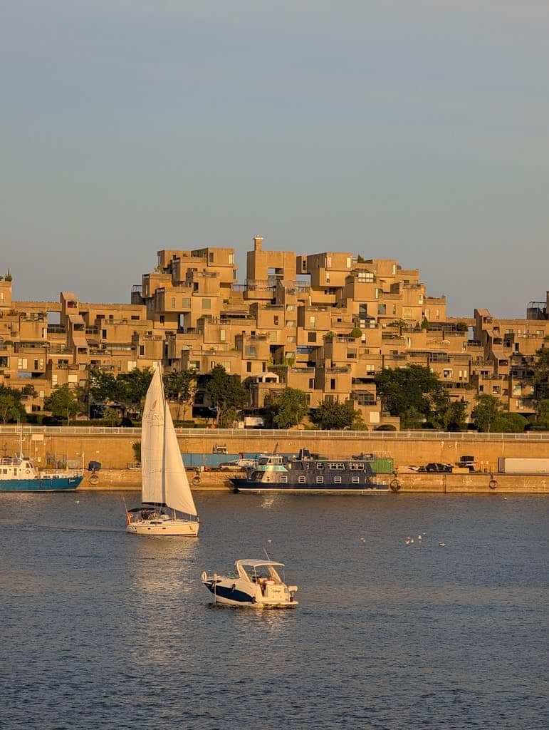 A scenic view of sailboats on the water near the iconic Habitat 67 in Montreal during a sunny day.