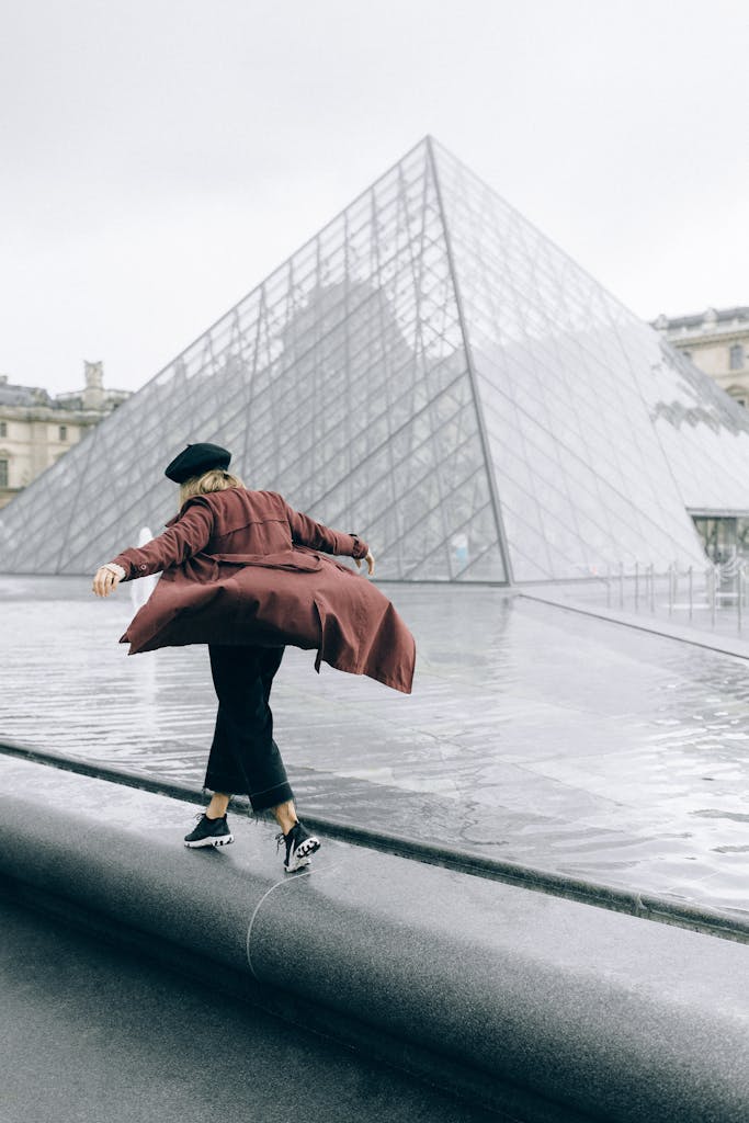 A woman with a beret enjoys a walk by the iconic Louvre Pyramid in Paris.