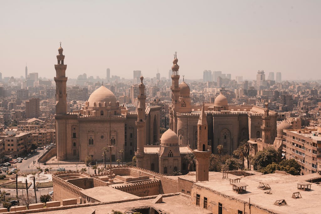 Aerial view of Cairo's historic mosques with a modern skyline backdrop under a clear sky.