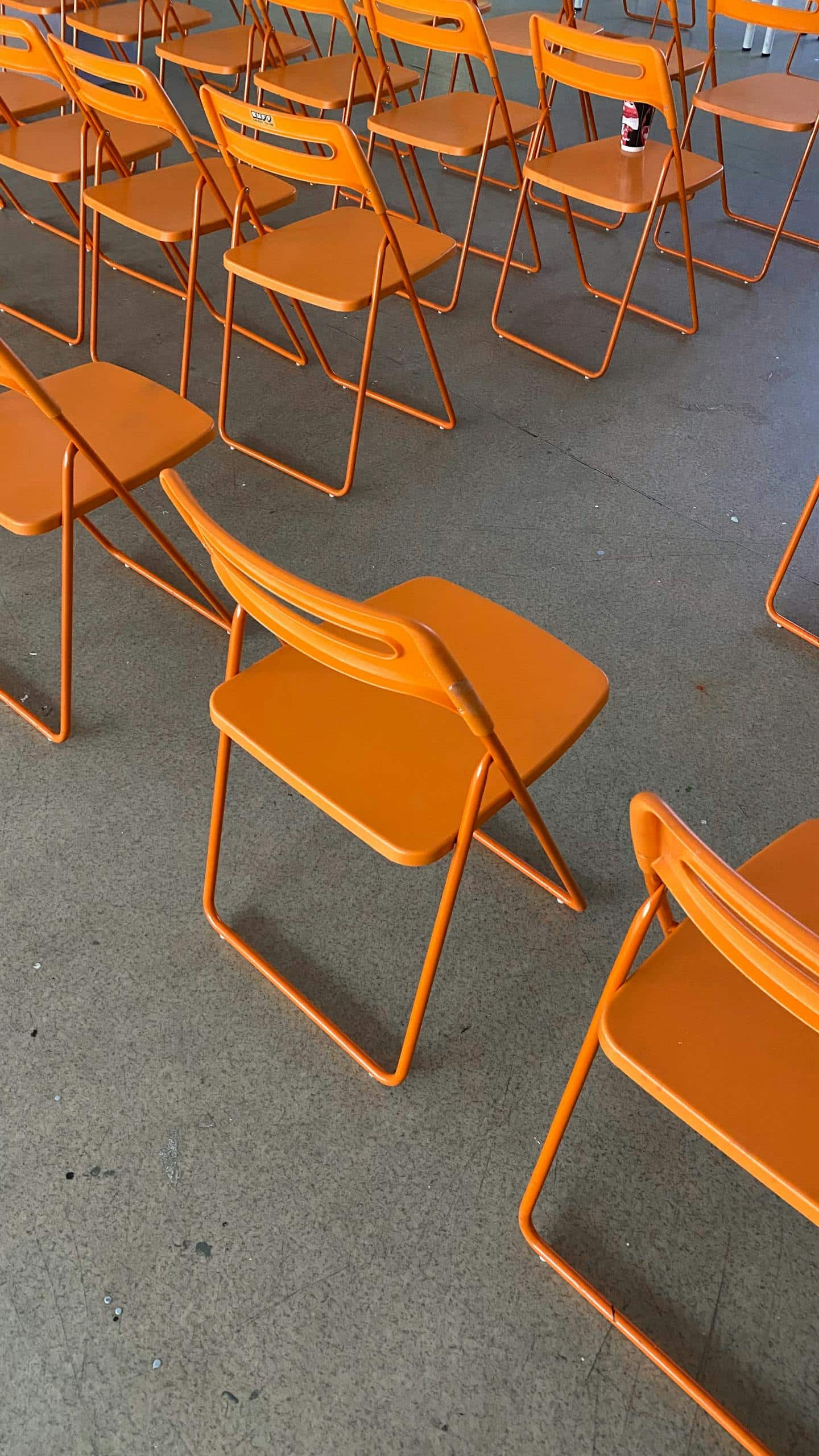 Bright orange folding chairs arranged in rows on a concrete floor, modern design.
