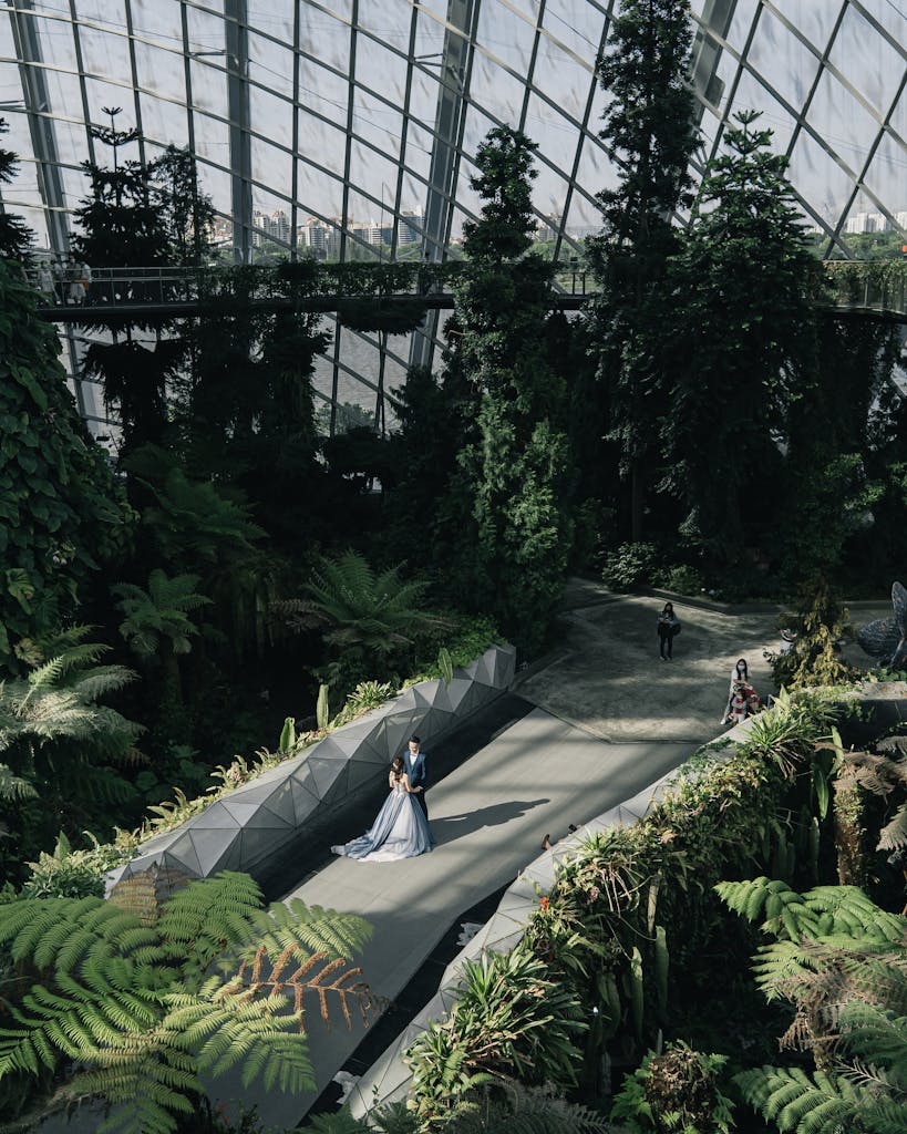 Couple posing amidst lush greenery in a modern indoor greenhouse setting.