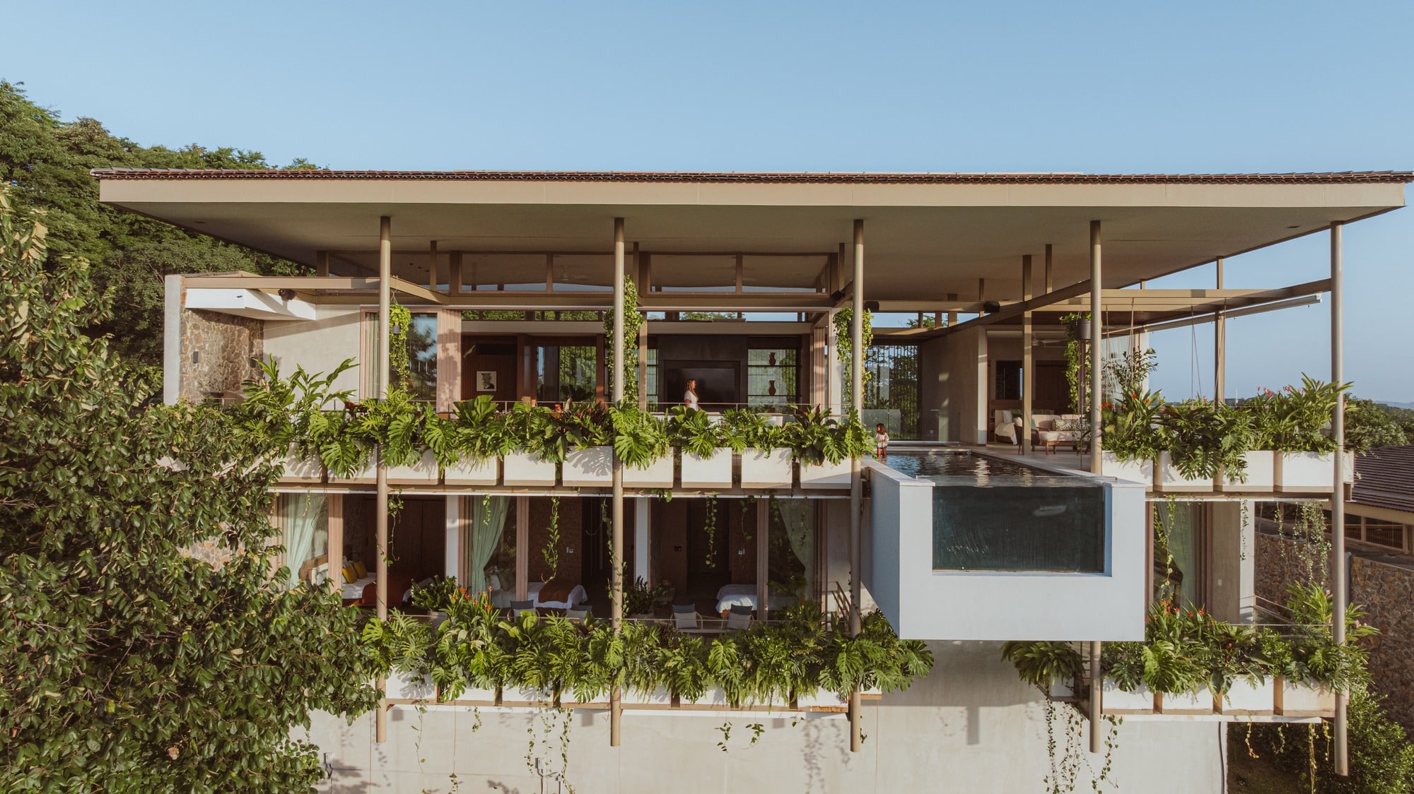 Exterior view of Nuri Villa showing seamless integration of indoor and outdoor spaces with green terraces and a suspended pool, emphasizing connection with nature.