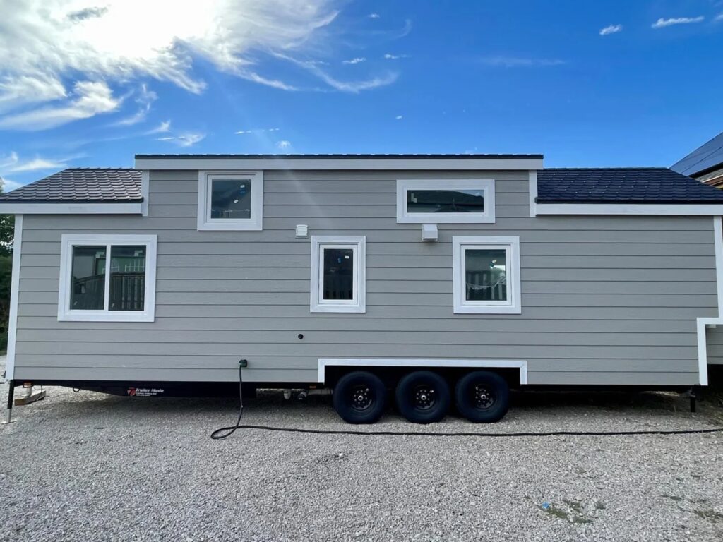 Exterior view of New Chapter tiny home on a triple-axle trailer, highlighting increased width and practical mobility for small-space living.
