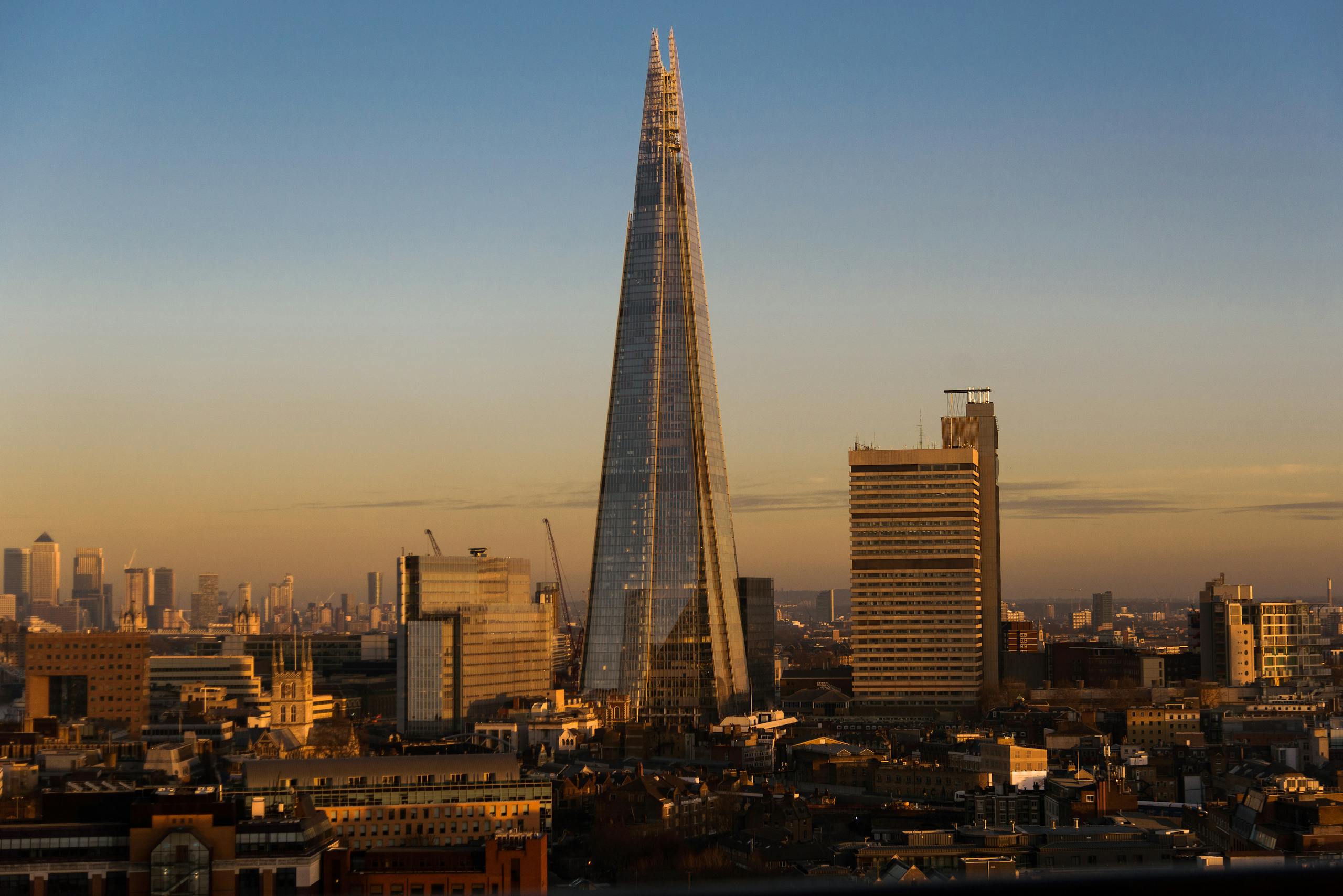 Modern futuristic skyscraper with creative design located on streets with residential buildings in London city in evening time against cloudless sky