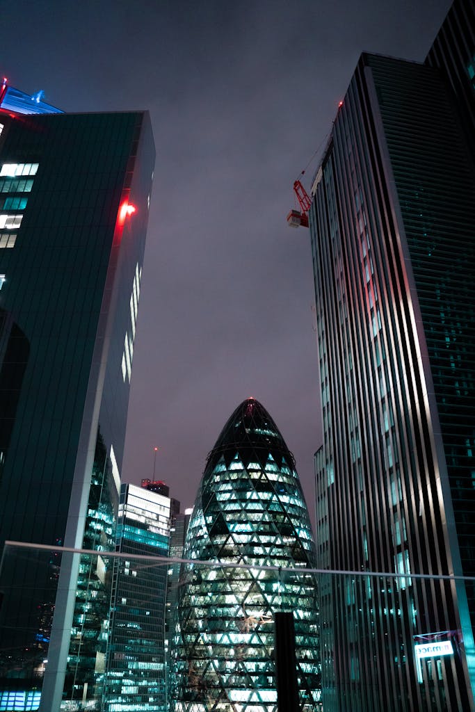 Modern skyscrapers in London's cityscape with the iconic Gherkin building illuminated at night.