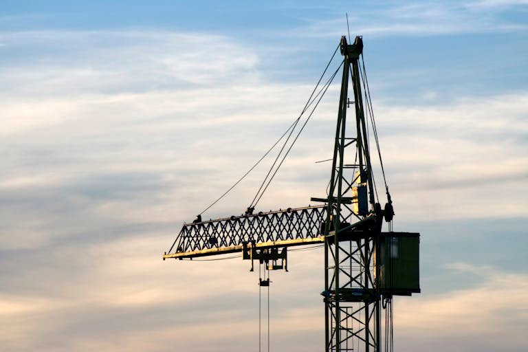 Silhouette of a construction crane set against a stunning sunset sky with soft clouds.