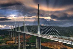 Silhouetted Millau Viaduct against a dramatic sunset sky with lightning in Occitanie, France.