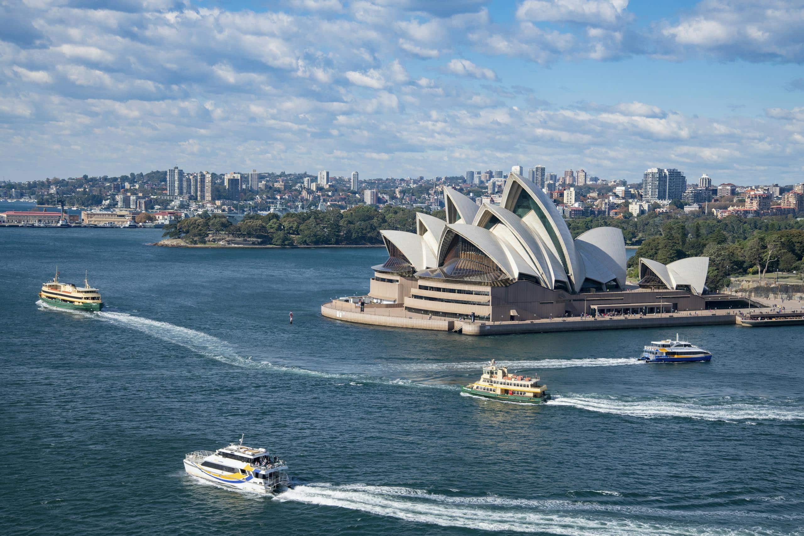 Stunning aerial photograph capturing Sydney Opera House and busy harbor ferries on a sunny day.
