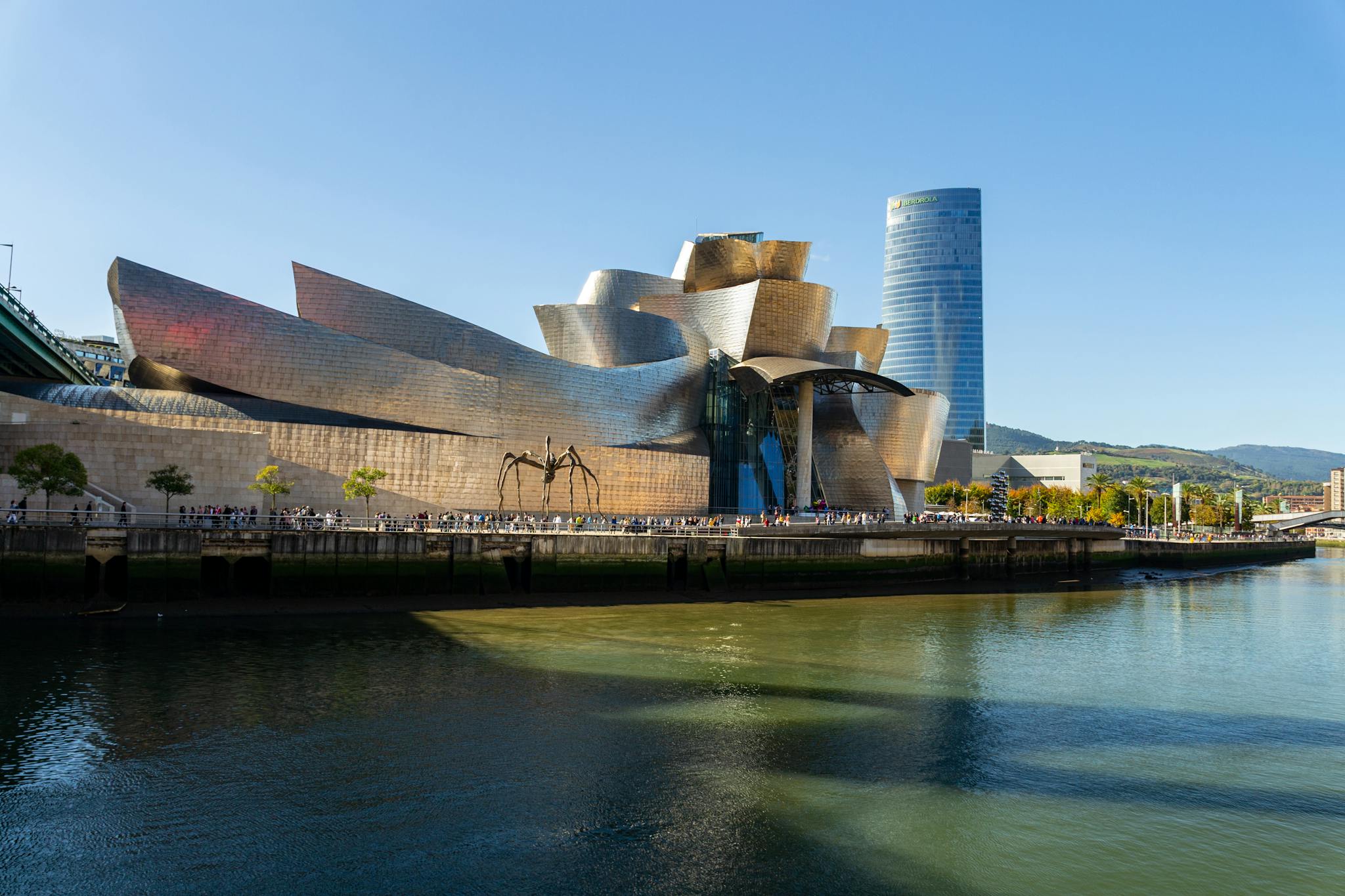 Stunning view of Guggenheim Museum Bilbao against a bright sky with reflective water.