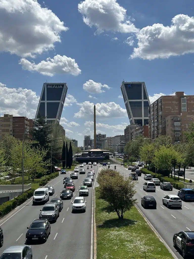 Traffic flows under Madrid's striking Gate of Europe towers on a sunny day.