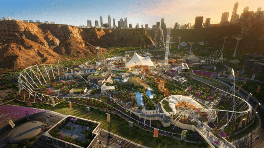 A wide aerial rendering of the Six Flags Qiddiya City theme park, showcasing various roller coasters, themed lands, and the central Citadel under a bright sky with the city skyline in the background.