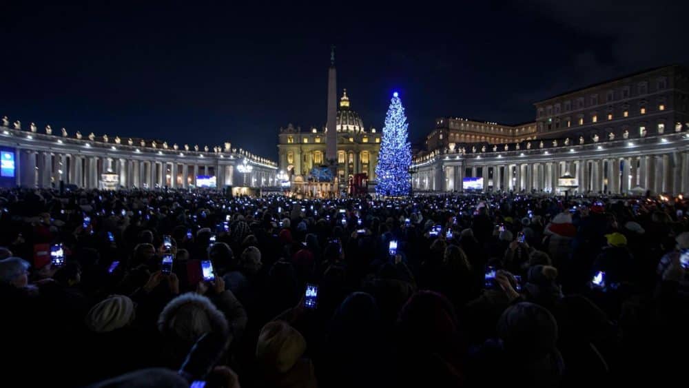Architecture and temporary installations in St. Peter&rsquo;s Square: Christmas tree and Nativity scene illuminated at night, with crowd capturing the festive urban experience.