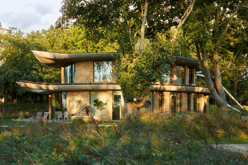 Curved stone fa&ccedil;ade harmonizes with trees; a feeling of seamless integration into the rural landscape.