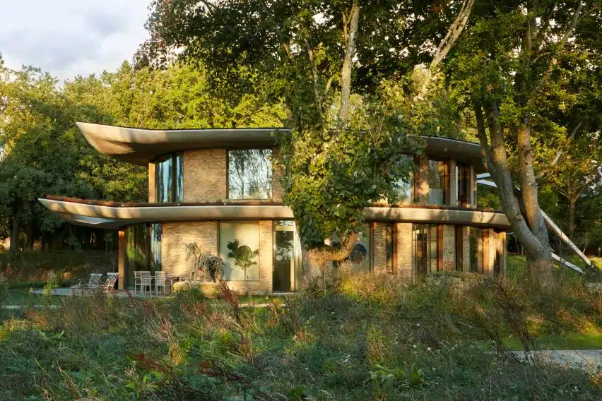 Curved stone fa&ccedil;ade harmonizes with trees; a feeling of seamless integration into the rural landscape.