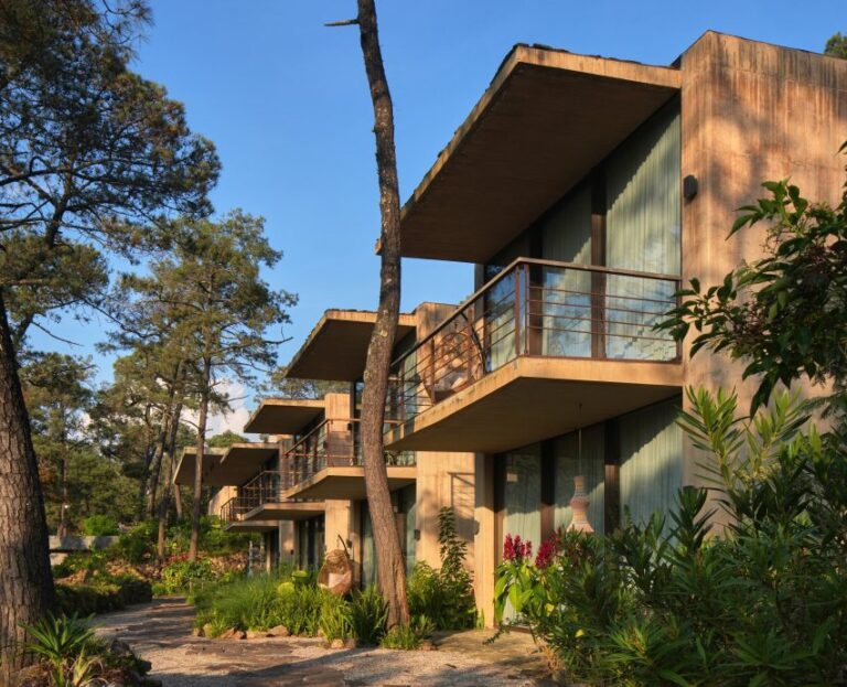 Exterior view showing the repetitive facades of the Segmented Concrete Pavilions at Rancho del Bosque, featuring shaded balconies and dense planting.