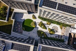 Expansive, geometrically designed upper courtyard situated between residential blocks, showcasing green roof design and solar panel coverage, reflecting the Vertical Integration of Industry and Housing project.