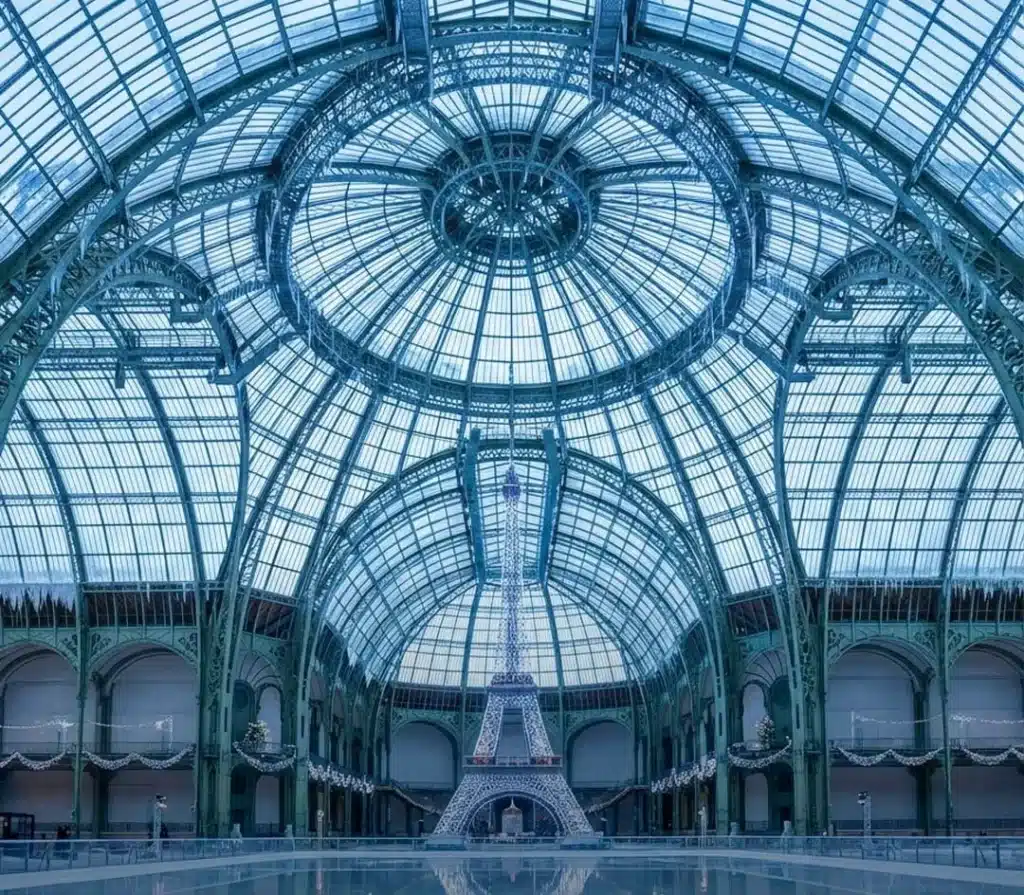 Eiffel Tower model at 1/10 scale stands amidst the calm ice rink under the Palace's glass roof.