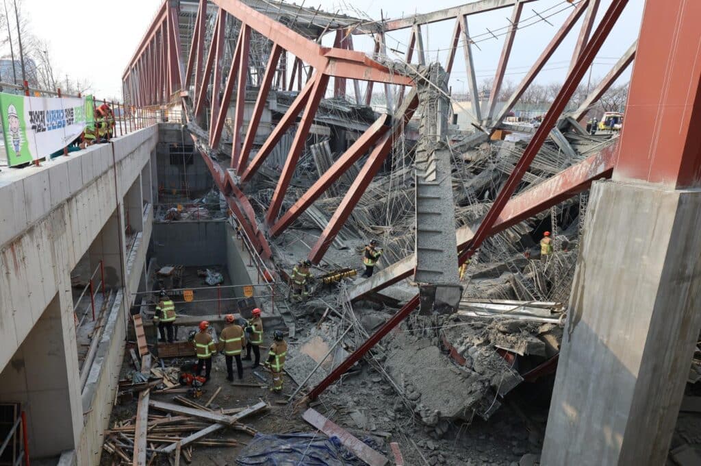 Scene of the structural collapse at the Gwangju City Main Library construction site, where firefighters inspect rubble amid red steel trusses and shattered concrete, following an accident that killed four workers.