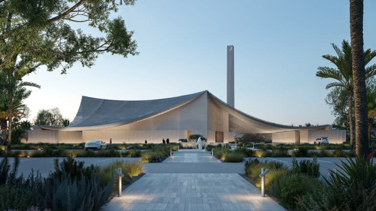 Exterior view of the Palm Jebel Ali Friday Mosque at dusk, featuring its sweeping textile-inspired canopy, 40-meter minaret with crescent moon finial, and landscaped approach path lined with native plants and palm trees.