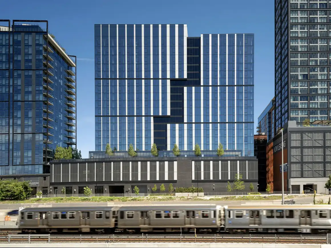 Coppia Tower in Chicago's West Loop, a 19-story mixed-use building with geometric glass façade, featuring an interstitial recess and surrounded by urban architecture under a clear blue sky.